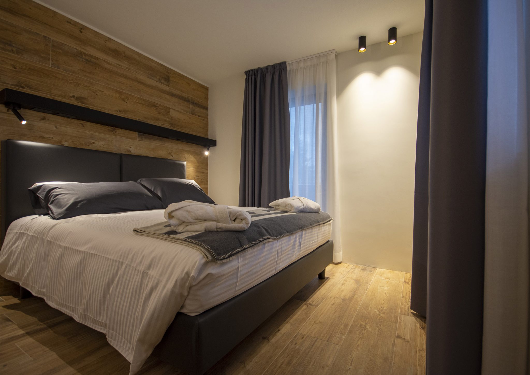 Hotel Rascard, vista angolare su camera letto con testata rivestita in ceramica effetto legno